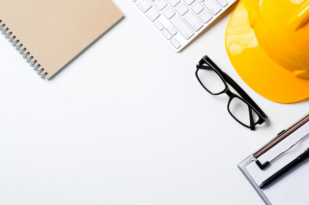 Escritorio de oficina de arquitecto con herramientas, casco, computadora, lentes y cuaderno.