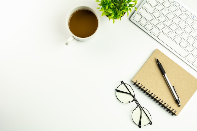 Escritorio de oficina blanco moderno con un teclado de computadora, una pluma, un cuaderno y una taza de café.