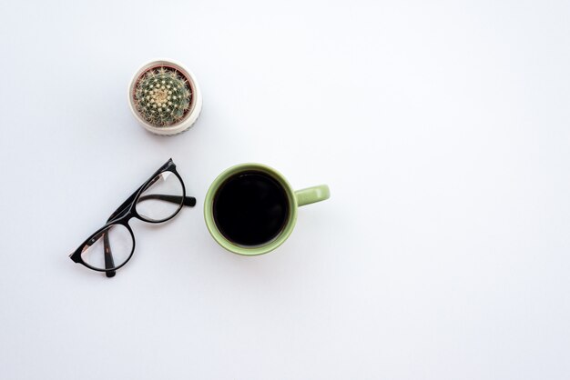 Escritorio de oficina blanco con vasos, taza de café y cactus.