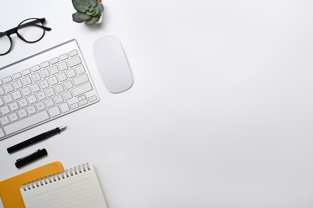 Escritorio de oficina blanco de vista superior con teclado inalámbrico, gafas, cuaderno y planta suculenta