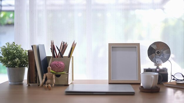 Escritorio de oficina en casa con computadora portátil planta en maceta cámara retro y taza de café