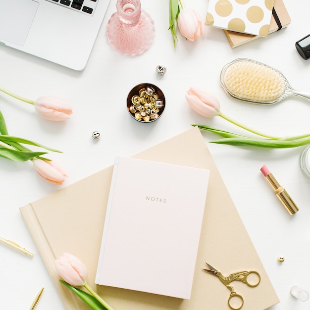 Escritorio de oficina en casa de mujer. Espacio de trabajo con laptop, flores de tulipán rosa, notebook, accesorios y cosméticos. Endecha plana, vista superior