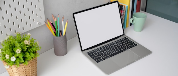 Escritorio de oficina en casa con pantalla en blanco portátil, papelería, libros y maceta en mesa blanca
