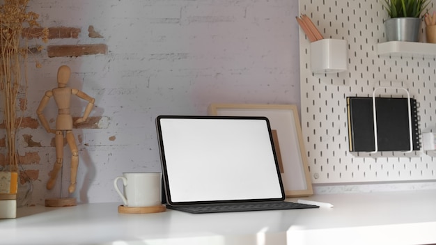 Escritorio de oficina en casa con tableta de pantalla en blanco con teclado inteligente en la mesa de espacio de trabajo mínimo.