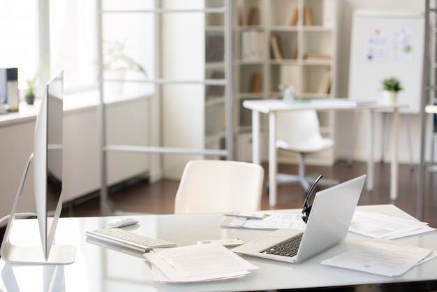 Escritorio de oficina con dos computadoras en la mesa con informes, dispositivo de manos libres en la computadora portátil