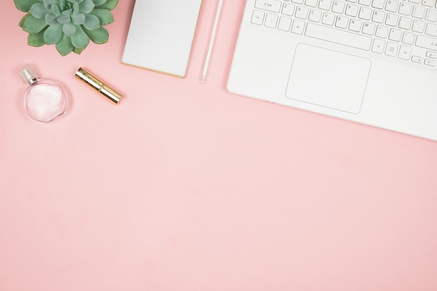 Foto escritorio de oficina femine con accesorios de oficina en superficie rosa. espacio de trabajo para mujeres con suculentas, velas y cosméticos.