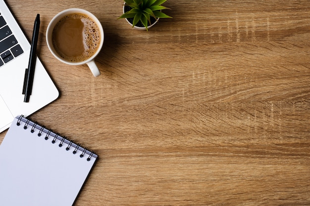 Escritorio de oficina con laptop, cuaderno en blanco y taza de café en la mesa de madera