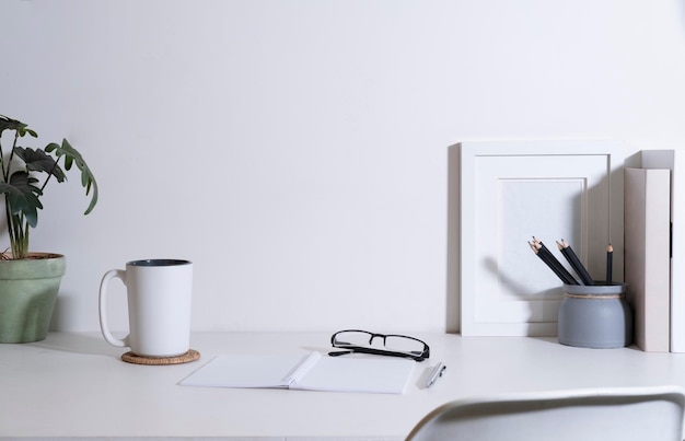 Escritorio de oficina con marco de imagen, taza de café, planta de interior y suministros en mesa blanca. Copiar espacio para el texto publicitario.