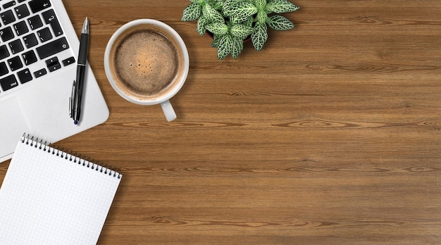 Escritorio de oficina moderno con computadora portátil, taza de café y bolígrafo sobre mesa de madera.