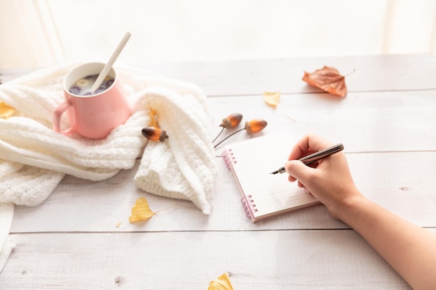 Escritorio de oficina moderno femenino con cuaderno rosa pastel, vasos, taza de café, flores silvestres