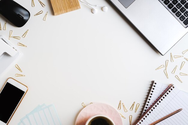 Escritorio de oficina con portátil, teléfono móvil, té en una taza rosa, clips de papel, pegatinas y auriculares