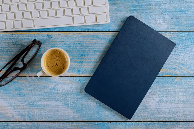 Escritorio de oficina con teclado, bloc de notas y taza de café y vasos.