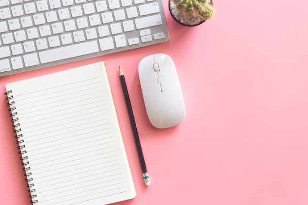 Escritorio rosa con cuaderno, mouse, teclado, cactus y lápiz