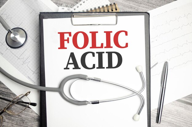El escritorio tiene un estetoscopio un bolígrafo azul y una carpeta de archivos gris con el texto ácido fólico