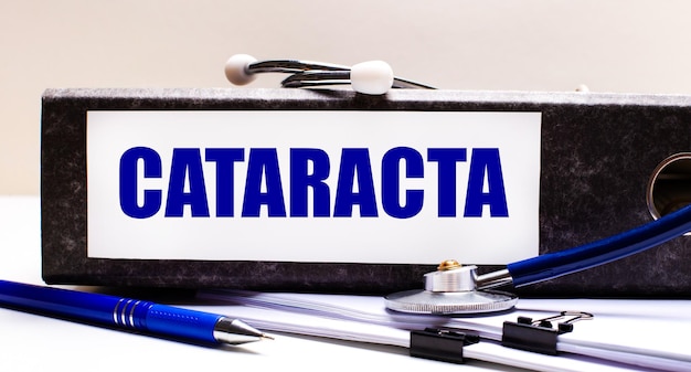 El escritorio tiene un estetoscopio, un bolígrafo azul y una carpeta gris con el texto CATARACT Medical concept