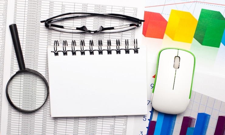 Foto el escritorio tiene una lupa, un mouse de computadora, gráficos en color, lentes y un cuaderno en blanco para pegar texto o ilustraciones. concepto de negocio