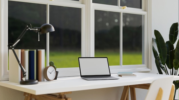 Escritorio de trabajo en casa mínimo contra la ventana con maqueta y decoración de computadora portátil portátil