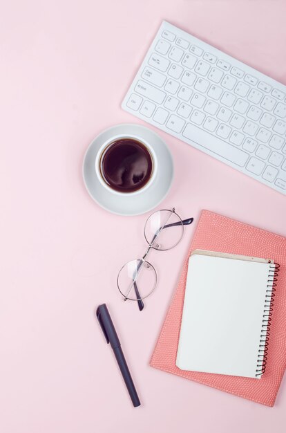 Escritorio de trabajo con cuadernos, espacio en blanco vacío, suministros, vasos y taza de café sobre fondo rosa. Vista superior con espacio para texto. Endecha plana. Oficina en casa de estilo minimalista o espacio de trabajo independiente moderno.