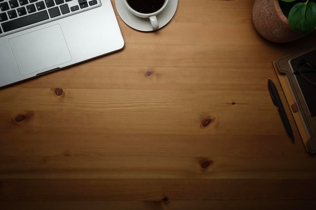 Escritorio de trabajo simple con computadora portátil, taza de café, cuaderno y planta de interior en la mesa de madera Vista superior con espacio para copiar