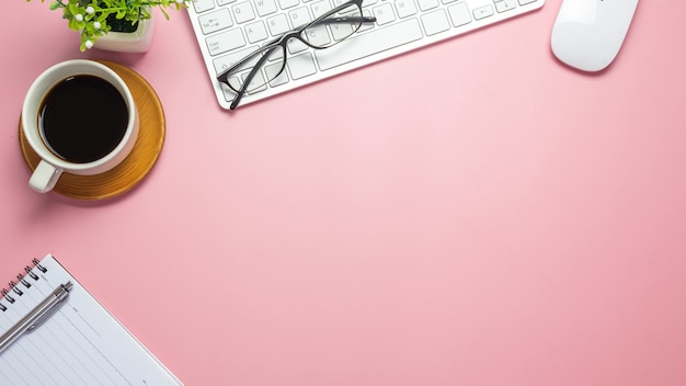 Escritorio con vasos de cuaderno de teclado de café sobre fondo rosa. Copie el espacio.