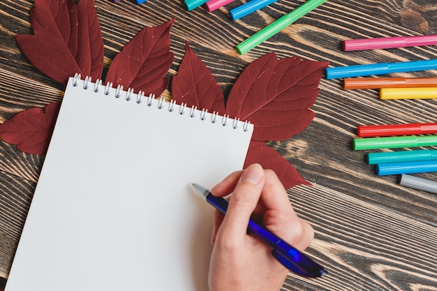 Escritura agradable de la mano femenina en cuaderno en blanco en la mesa de madera