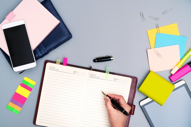 Escritura de la mano en el cuaderno rodeado de accesorios de oficina.