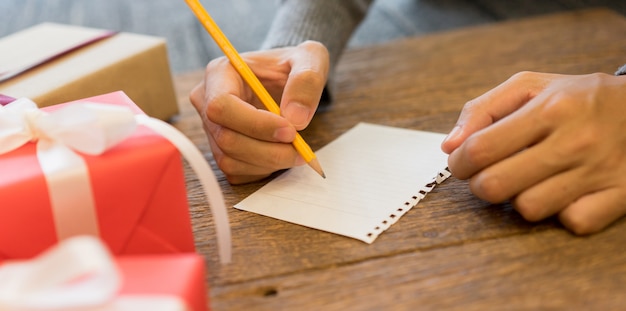 Escritura de la mano del hombre en el papel para la lista de deseos en el escritorio de madera de la tabla con la caja de regalo