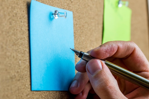 Foto escritura a mano masculina en una hoja en blanco de papel azul con espacio de copia anclado en un tablón de anuncios de corcho.