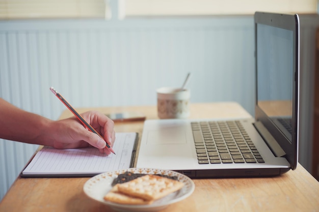 Escritura a mano recortada en el diario por computadora portátil en la mesa