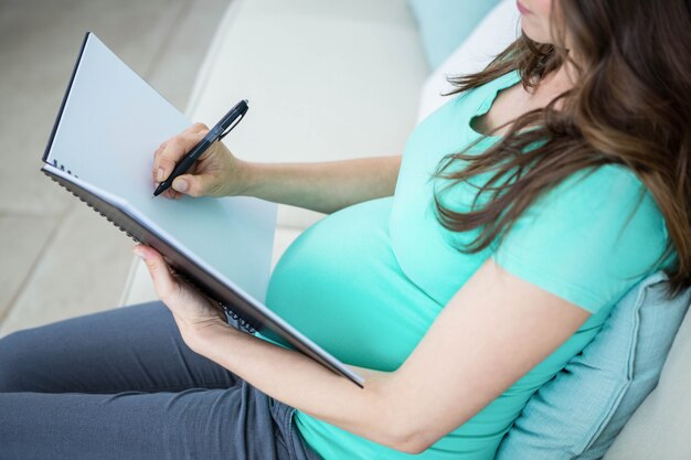 Foto escritura de la mujer embarazada en el documento en el sofá