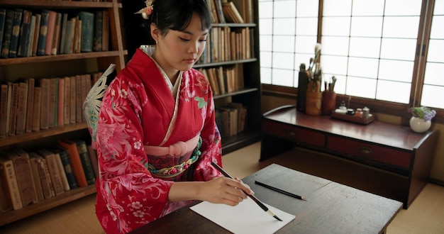 Escritura con tinta y mujer japonesa en casa para escritura tradicional en documentos de papel y página Cultura creativa asiática y persona con herramientas de pincel vintage para caligrafía fuente y texto en casa