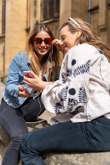 Escuchando música en la ciudad dos amigas caucásicas sonriendo y compartiendo auriculares y escuchando música en streaming