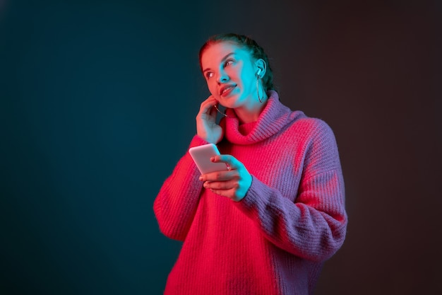 Escuche música, soñadora. Retrato de mujer caucásica aislado sobre fondo de estudio degradado en luz de neón. Modelo de mujer hermosa con el pelo rojo. Concepto de emociones humanas, expresión facial, anuncio.