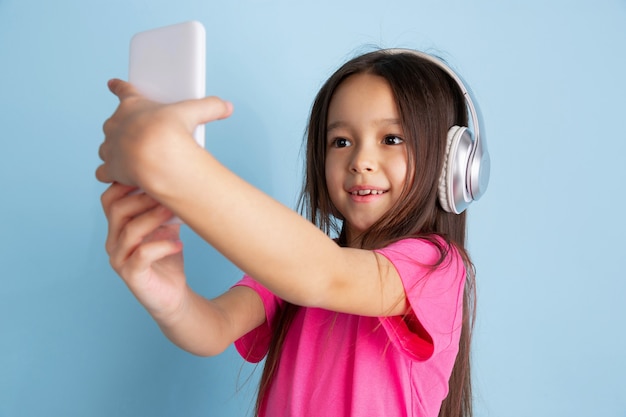 Foto escuche música, tome selfie. retrato de niña caucásica en la pared azul.