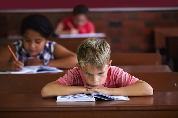 La escuela apesta Un niño que descansa su cabeza sobre sus brazos mientras se sienta en un salón de clases con aspecto aburrido