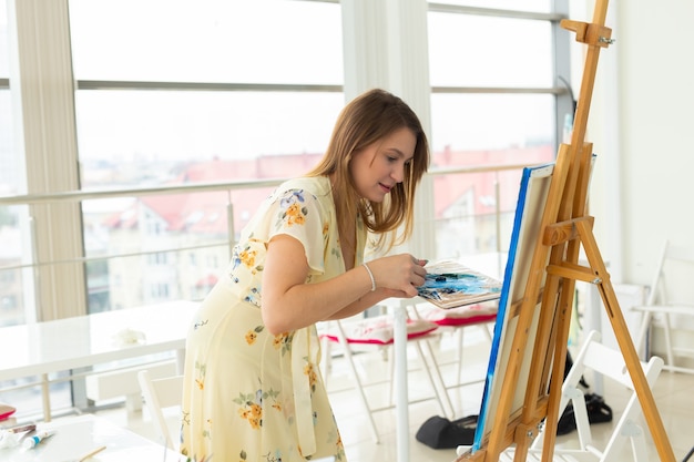 Escuela de arte, creatividad y concepto de ocio - niña estudiante o artista joven con caballete, paleta y pintura de pincel en el estudio