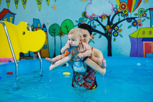 Foto escuela para enseñar a los niños a nadar un niño de nueve meses está aprendiendo a nadar en la piscina con un entrenador