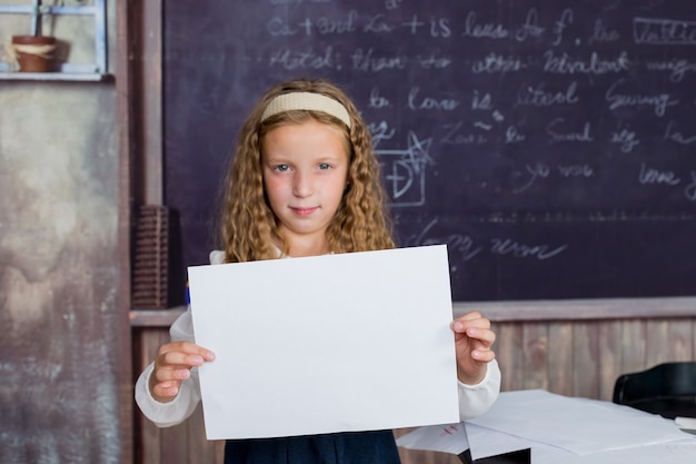 La escuela es un lugar feliz niño pequeño feliz con papel en blanco sobre fondo de pizarra niña h ...