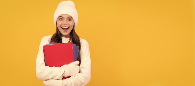 Foto escuela de invierno niño asombrado en gorro de invierno y guantes regreso a la escuela niño con libro de trabajo sobre fondo amarillo retrato de colegiala estudiante estudio banner encabezado escuela niño cara copyspace