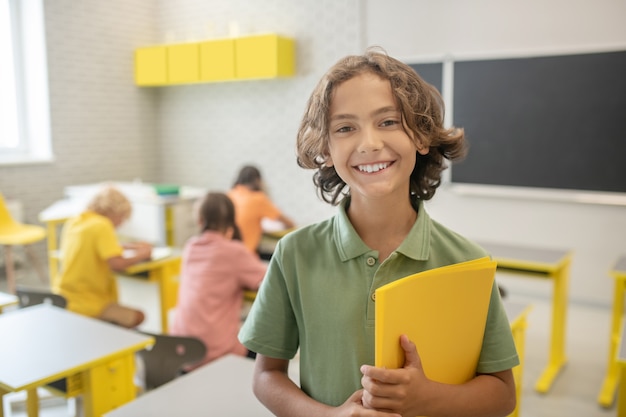 En la escuela. Lindo colegial en camiseta verde sonriendo muy bien