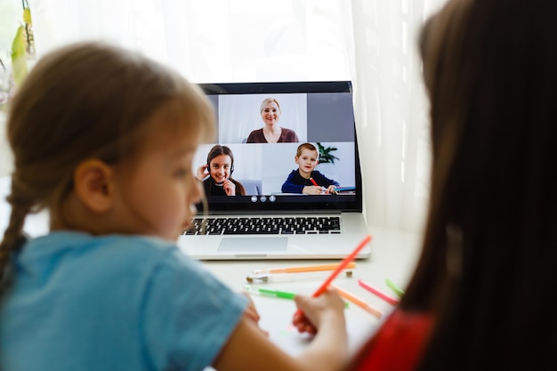 Escuela en línea genial. Niños que estudian en línea en casa usando una computadora portátil. Niñas alegres que usan la computadora portátil que estudian a través del sistema de e-learning en línea. Aprendizaje a distancia o remoto