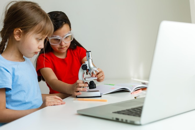 Escuela en línea genial. Niños que estudian en línea en casa usando una computadora portátil. Niñas alegres que usan la computadora portátil que estudian a través del sistema de e-learning en línea. Aprendizaje a distancia o remoto