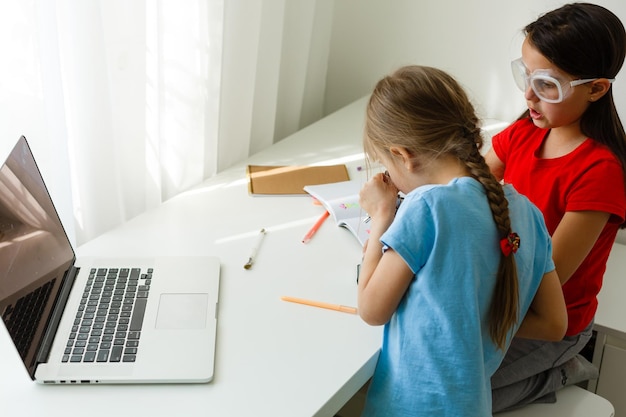 Escuela en línea genial. Niños que estudian en línea en casa usando una computadora portátil. Niñas alegres que usan la computadora portátil que estudian a través del sistema de e-learning en línea. Aprendizaje a distancia o remoto