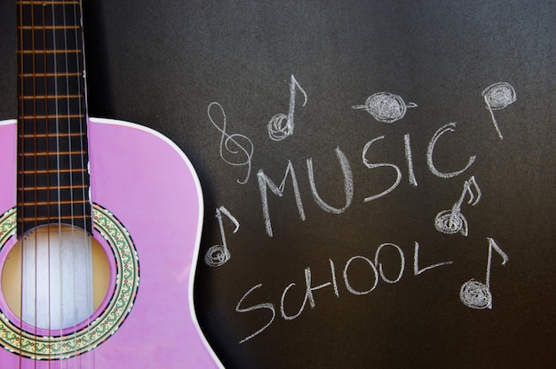 Foto escuela de música para niños con primer plano de guitarra púrpura sobre fondo de pizarra