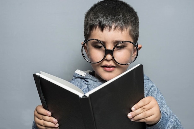 Escuela, niño con gafas gigantes leyendo un libro con gestos divertidos y variados