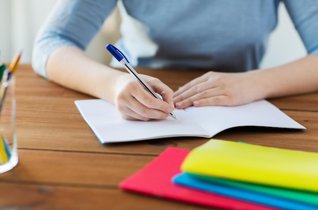 escuela secundaria, educación, personas y concepto de aprendizaje - cierre de estudiante o mujer escribiendo en un cuaderno en casa