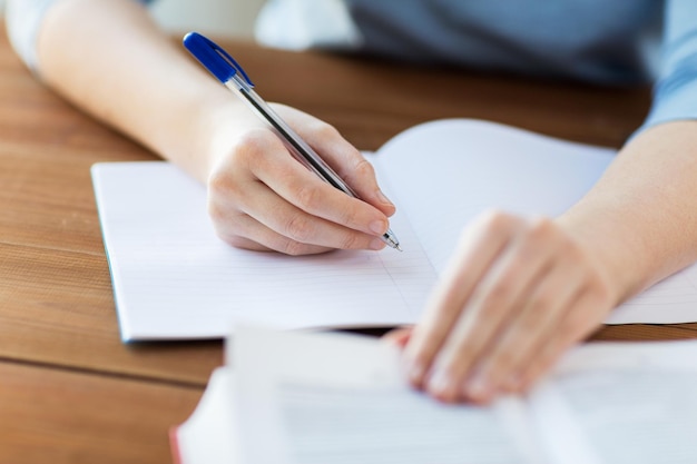 escuela secundaria, educación, personas y concepto de aprendizaje - cierre de una joven estudiante o mujer con un libro escribiendo en un cuaderno en casa