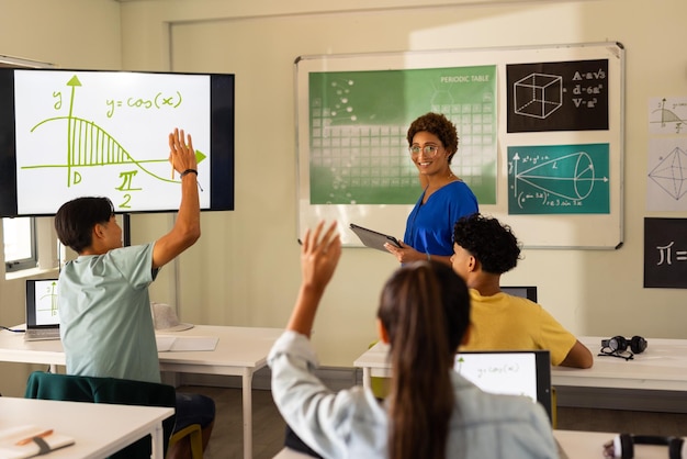 En la escuela secundaria los estudiantes levantan las manos en el aula mientras el maestro explica la lección de matemáticas