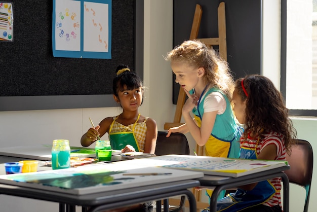 Foto en la escuela, tres niñas se centran en la pintura en la clase de arte.