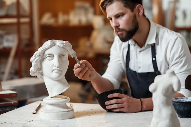 Escultor reparando escultura de gesso de cabeça de mulher no local de trabalho na área criativa